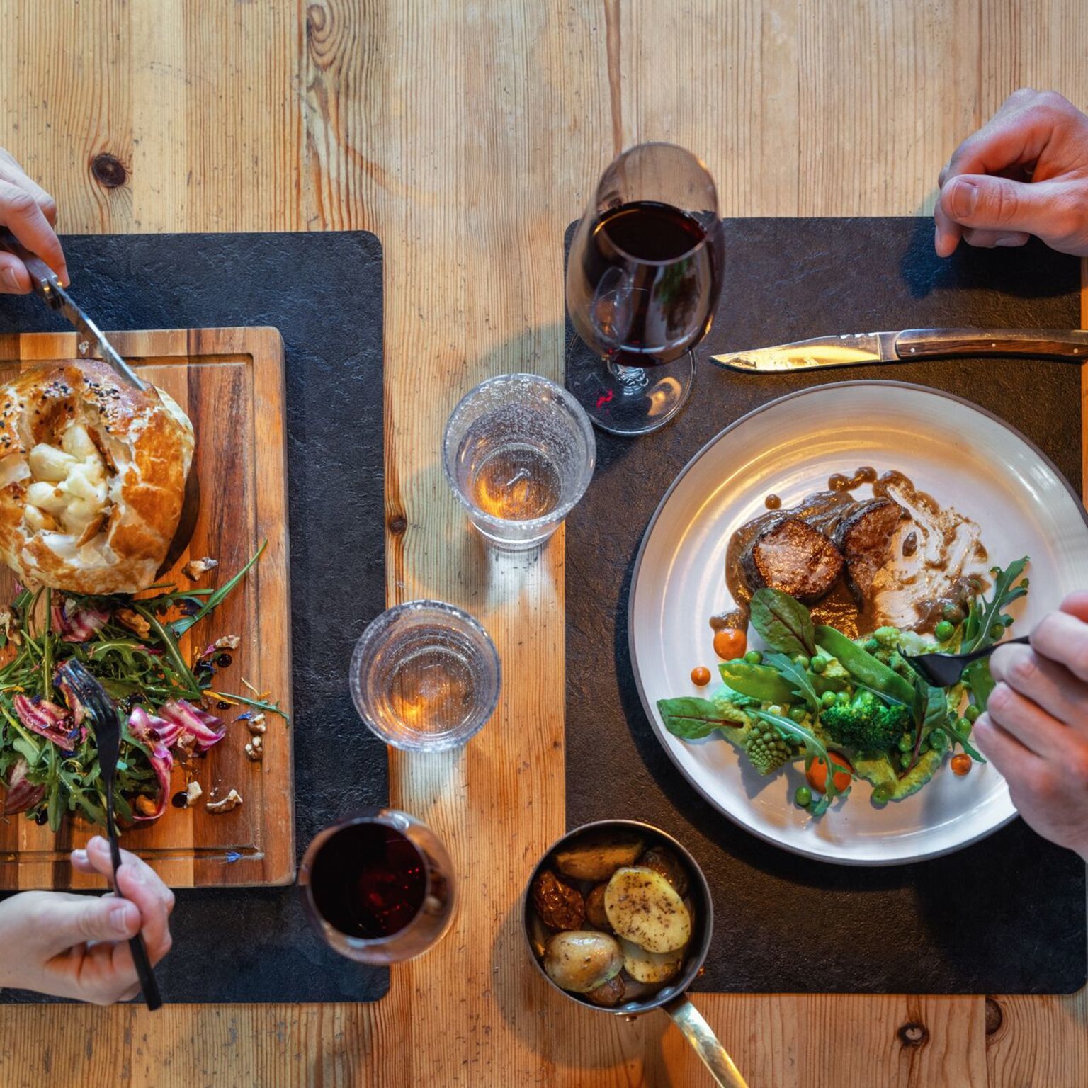 Two people enjoying a dinner with Valaisan specialties in a restaurant in Champéry, with meat, vegetables, potatoes, and red wine