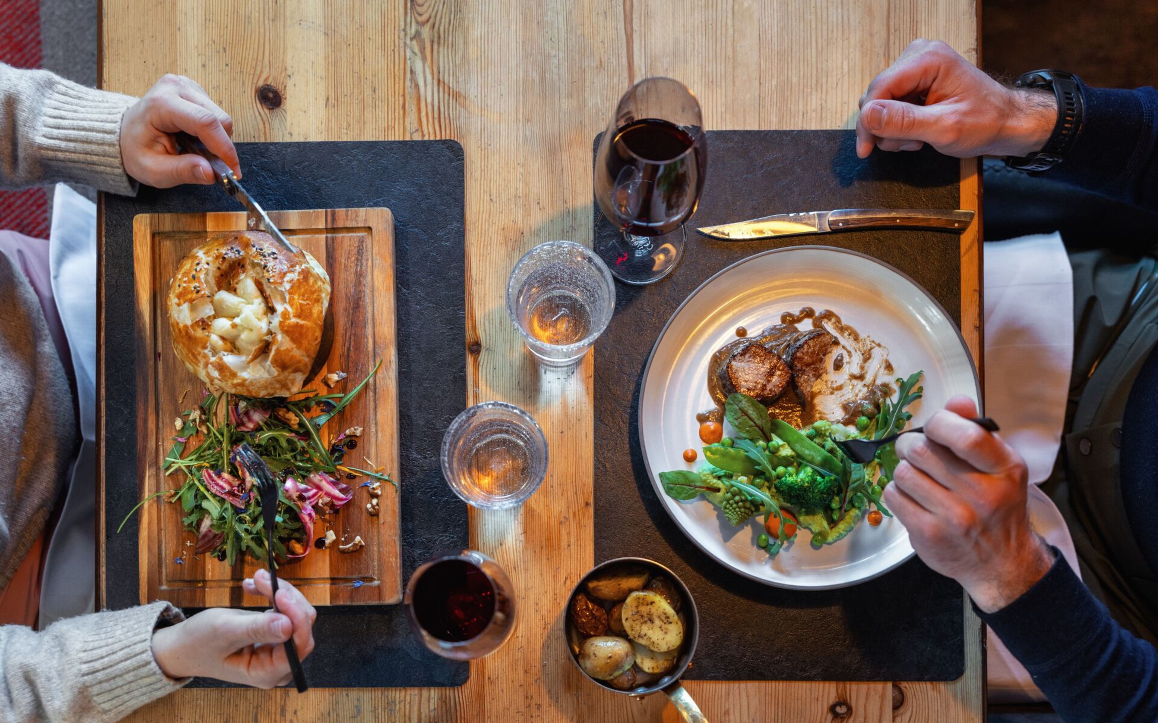 Deux personnes dégustent un dîner aux spécialités valaisannes dans un restaurant à Champéry, avec viande, légumes, pommes de terre et vin rouge
