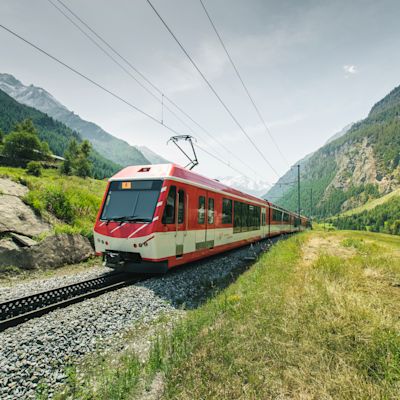 Train rouge de la Matterhorn Gotthard Bahn traversant le village de Randa en Valais, entouré de montagnes