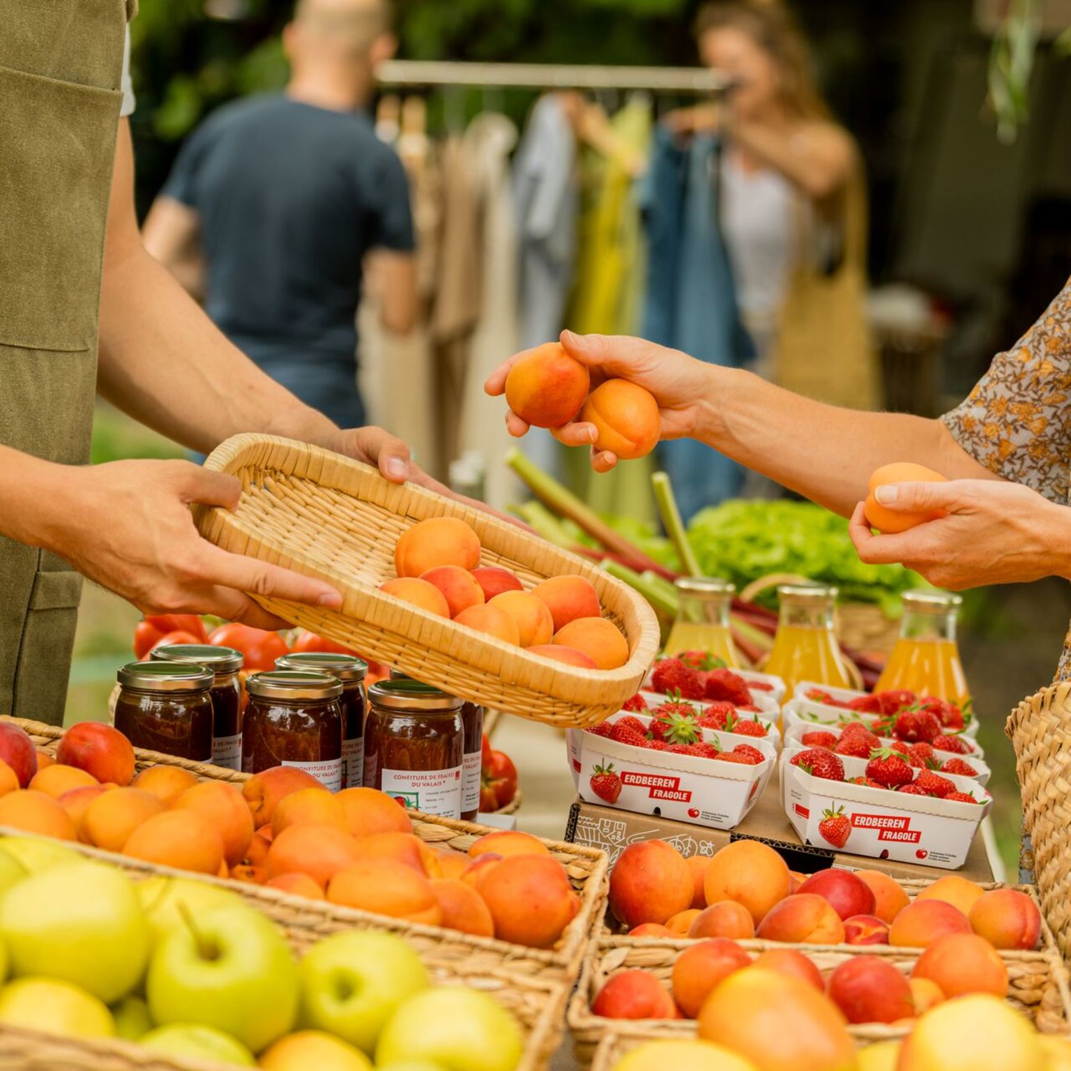 Personen kaufen frische Walliser Früchte und regionale Produkte an einem Marktstand