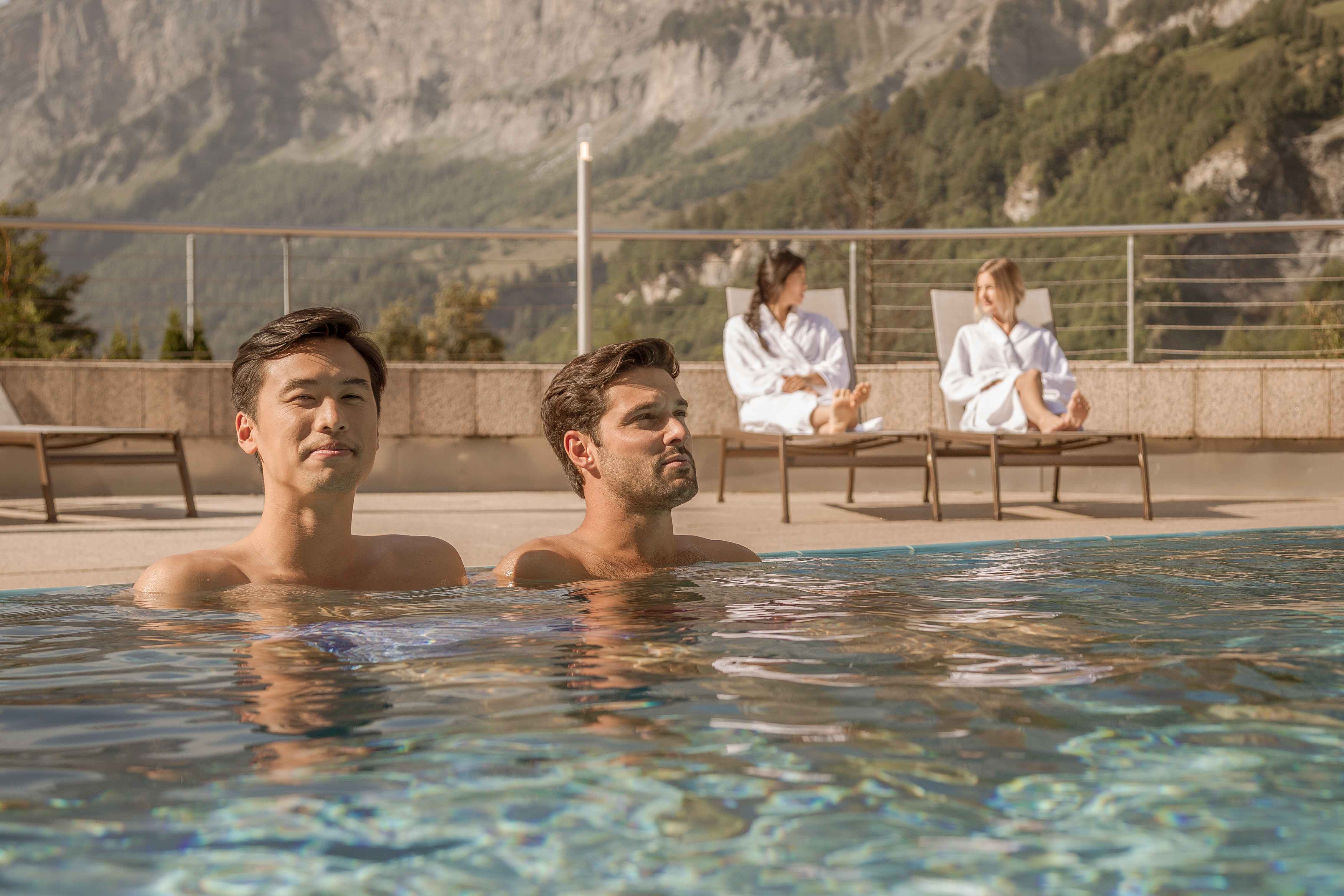 Two men enjoy the hot water of the baths while two women are on sunbeds in Leukerbad. Valais, Switzerland