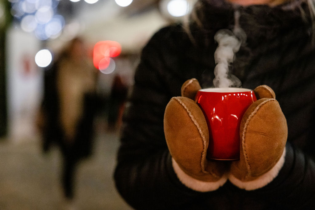 Personne avec des moufles tenant une tasse rouge fumante de vin chaud au marché de Noël de Brigue