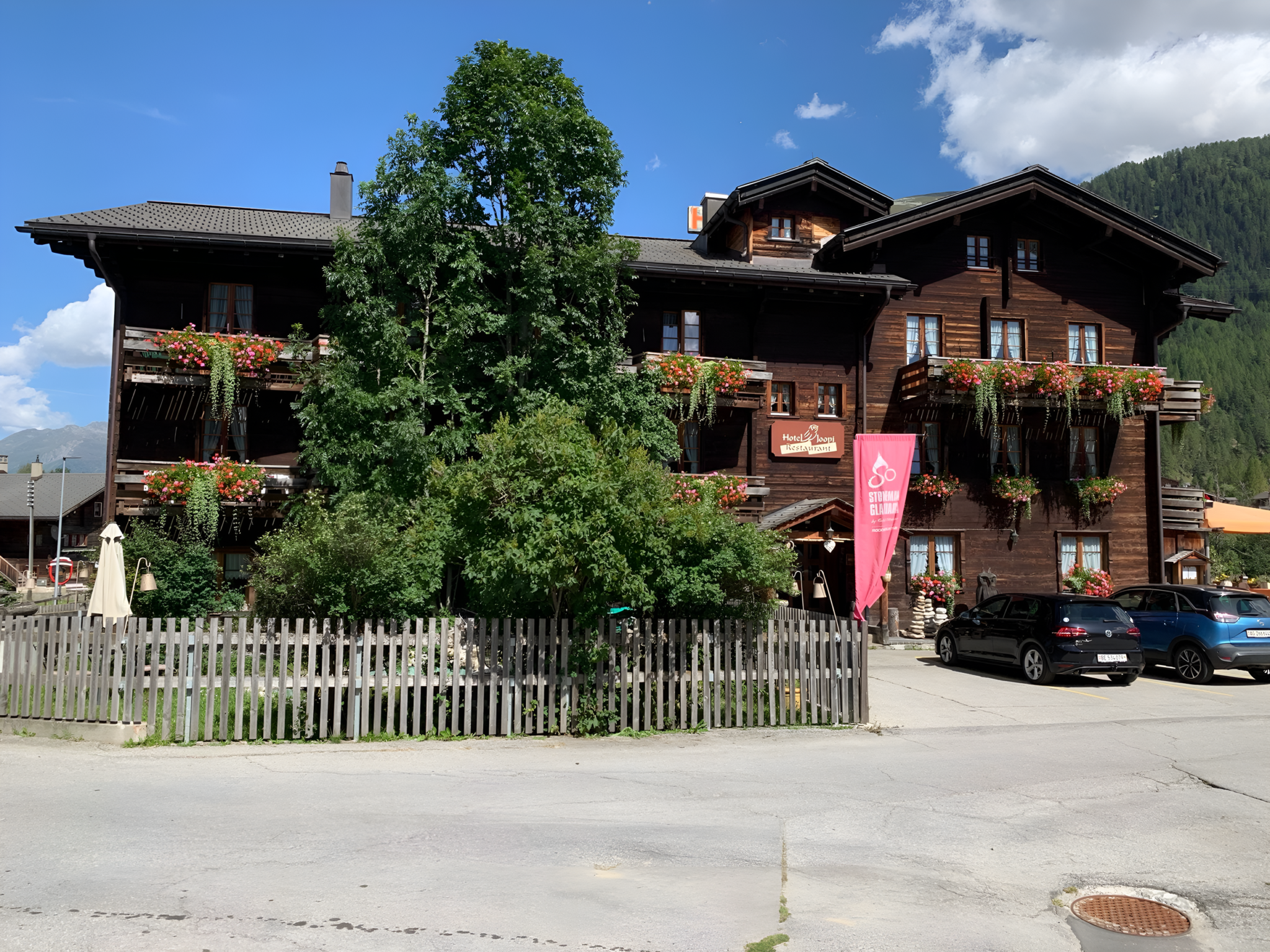Traditionelles Holzgebäude des Hotels Joopi in Reckingen mit Blumenbalkonen und Garten im Sommer