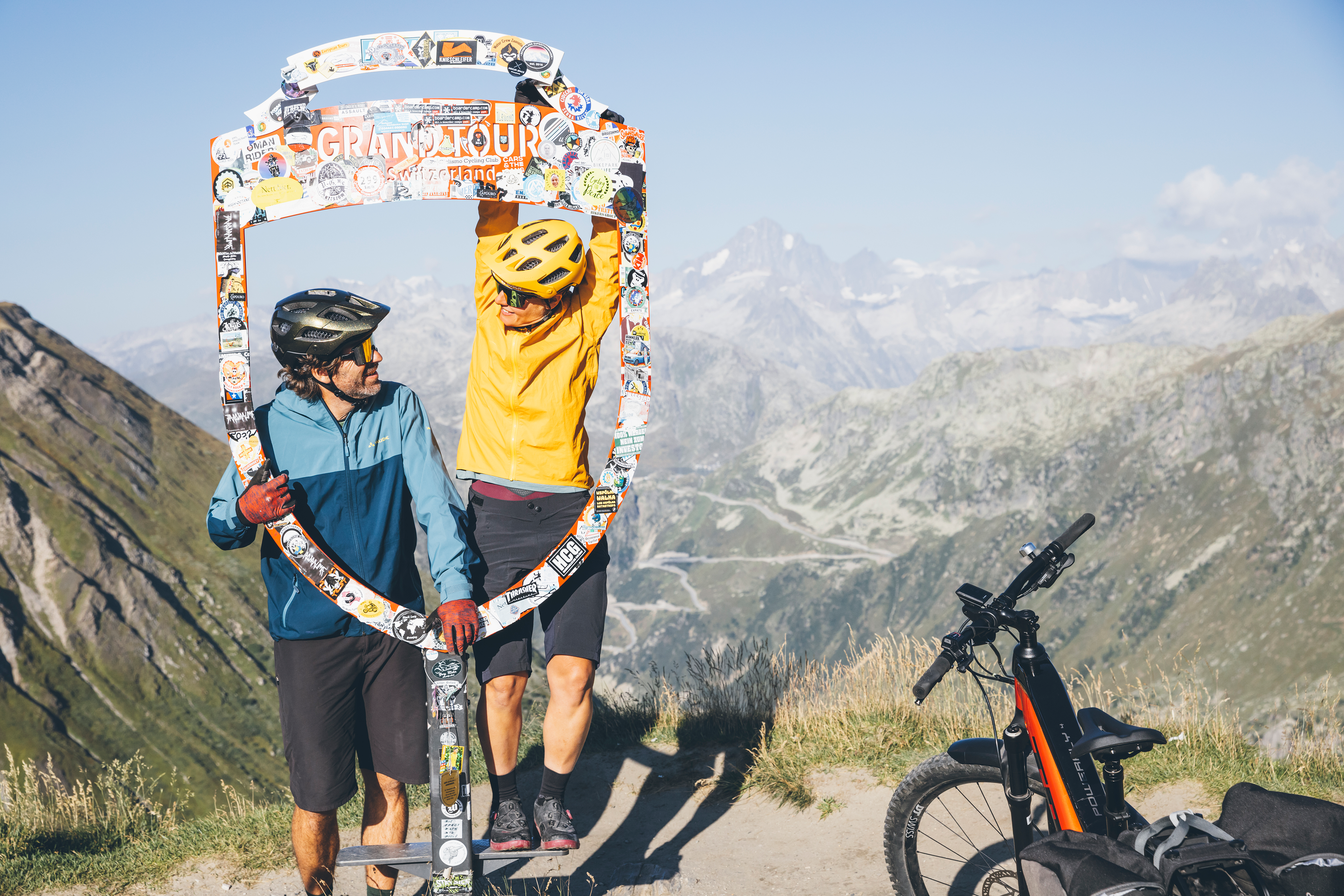 Two mountain bikers posing at the Grand Tour photo frame with alpine panorama in the background at the Furka Pass, Valais, Switzerland