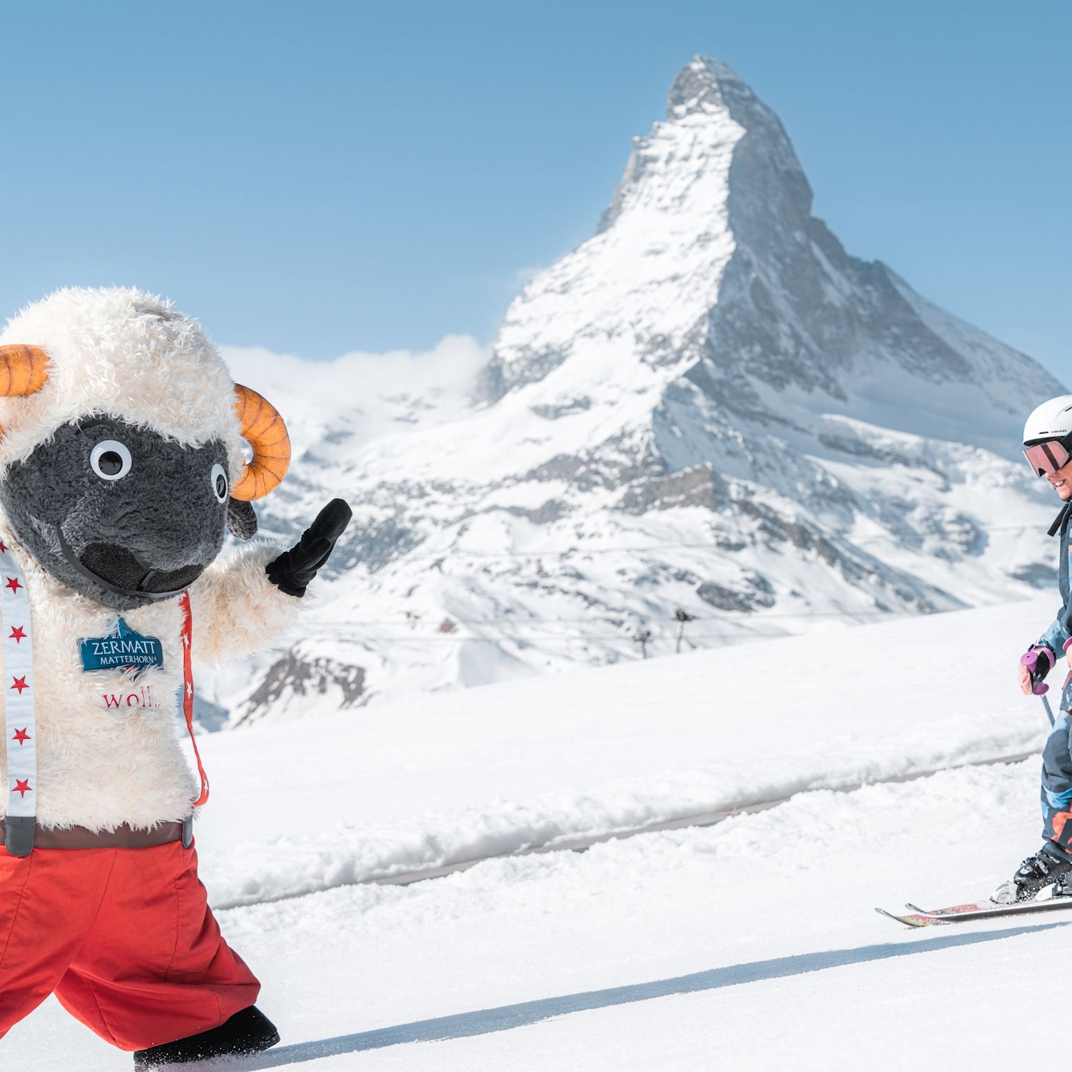Skifahrendes Kind mit Wolli-Maskottchen und dem Matterhorn im Hintergrund