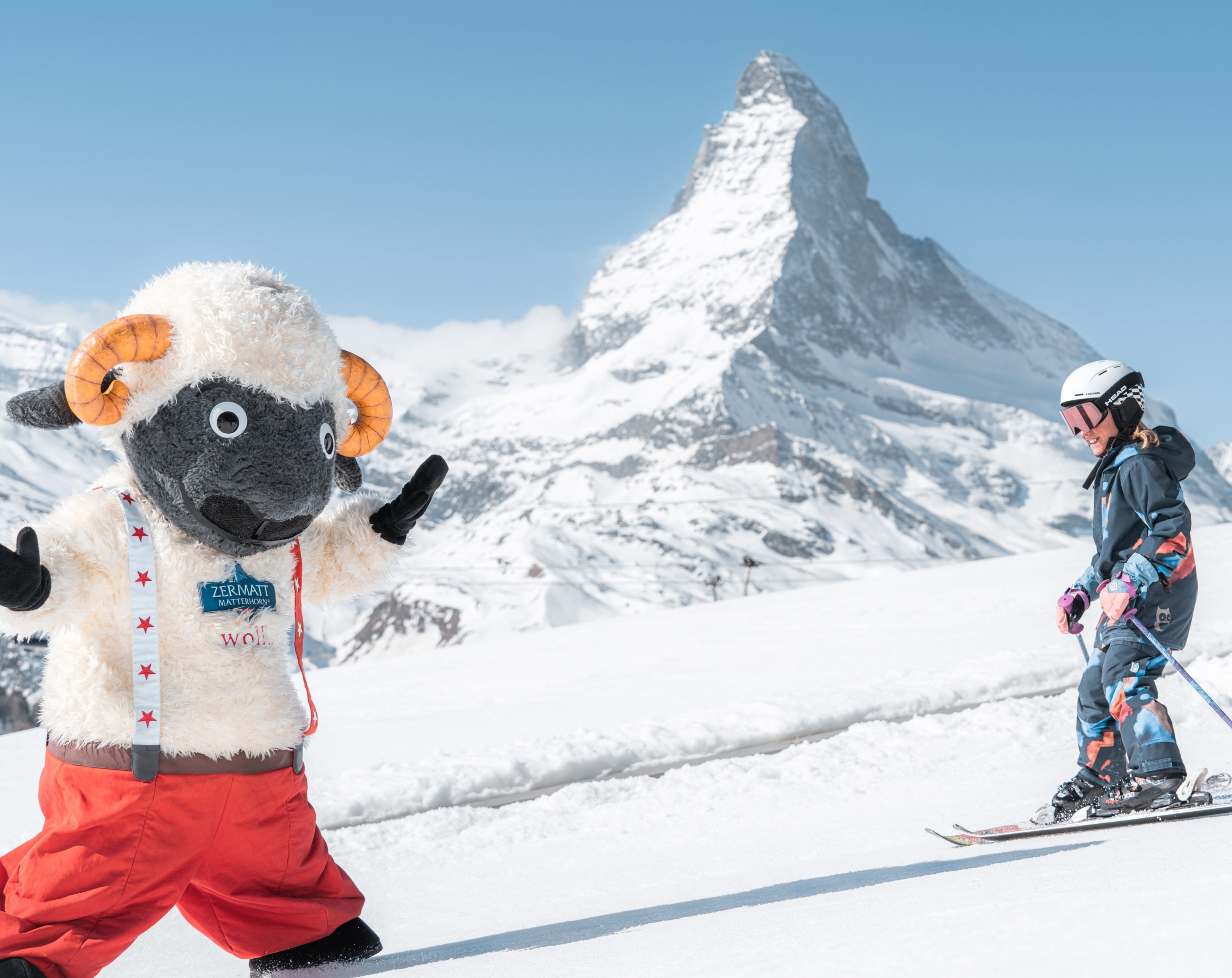 Skifahrendes Kind mit Wolli-Maskottchen und dem Matterhorn im Hintergrund
