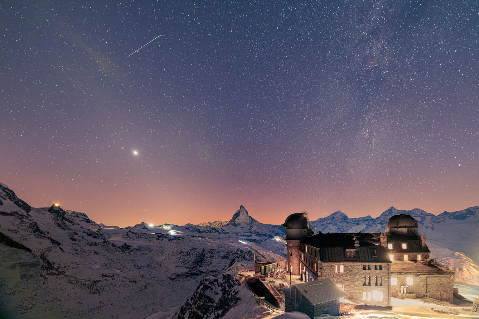 Vue nocturne depuis le Gornergrat avec le Kulmhotel illuminé et un ciel étoilé au-dessus du Cervinn