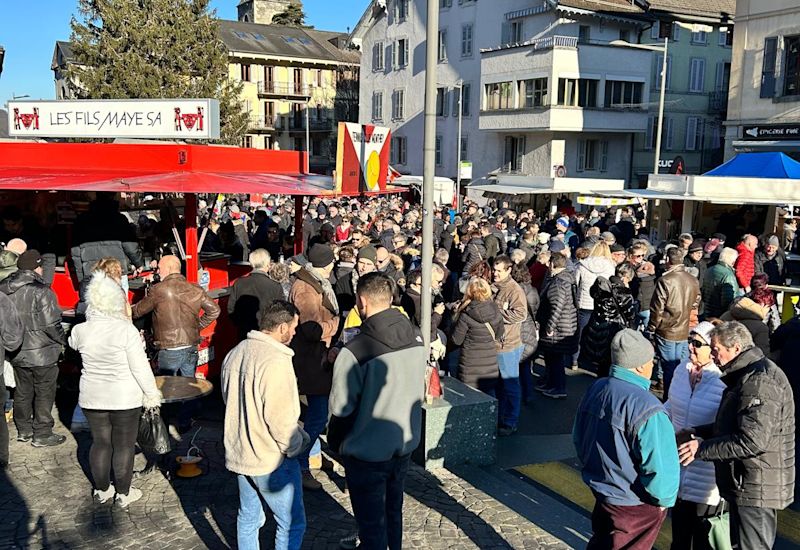 Menschenmenge auf der Place Centrale in Monthey mit Musik, Essensständen und festlicher Stimmung beim Silvestermarkt