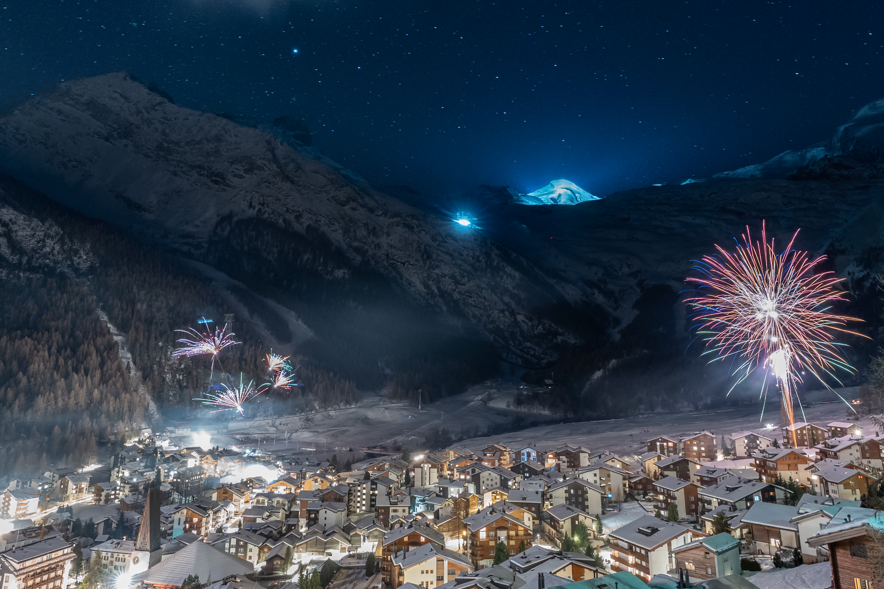 Feu d’artifice nocturne à Saas-Fee au-dessus des toits enneigés, avec les montagnes en toile de fond et une ambiance festive de Nouvel An