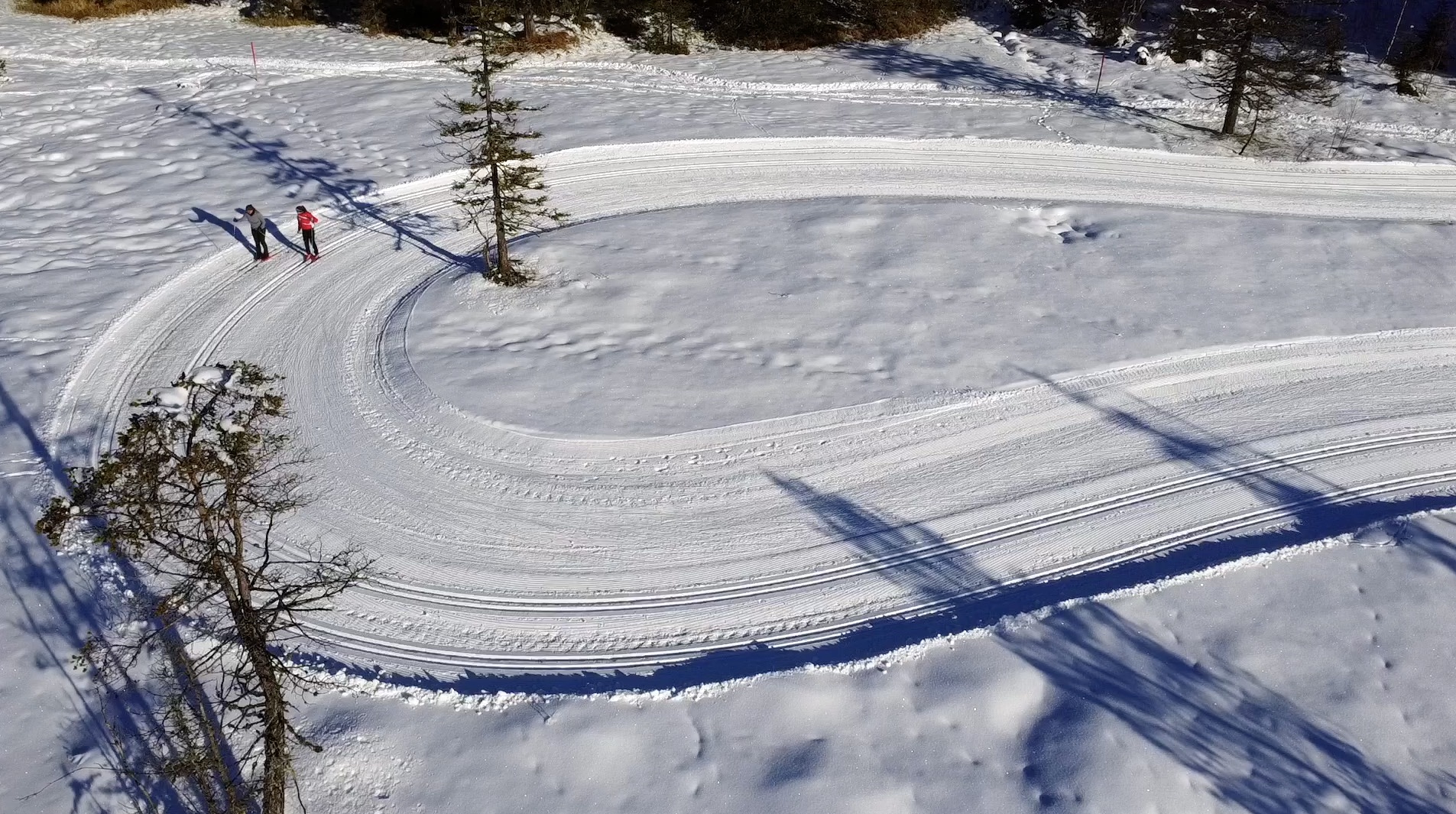 Two cross-country skiers seen from a drone in a bend in the trail 