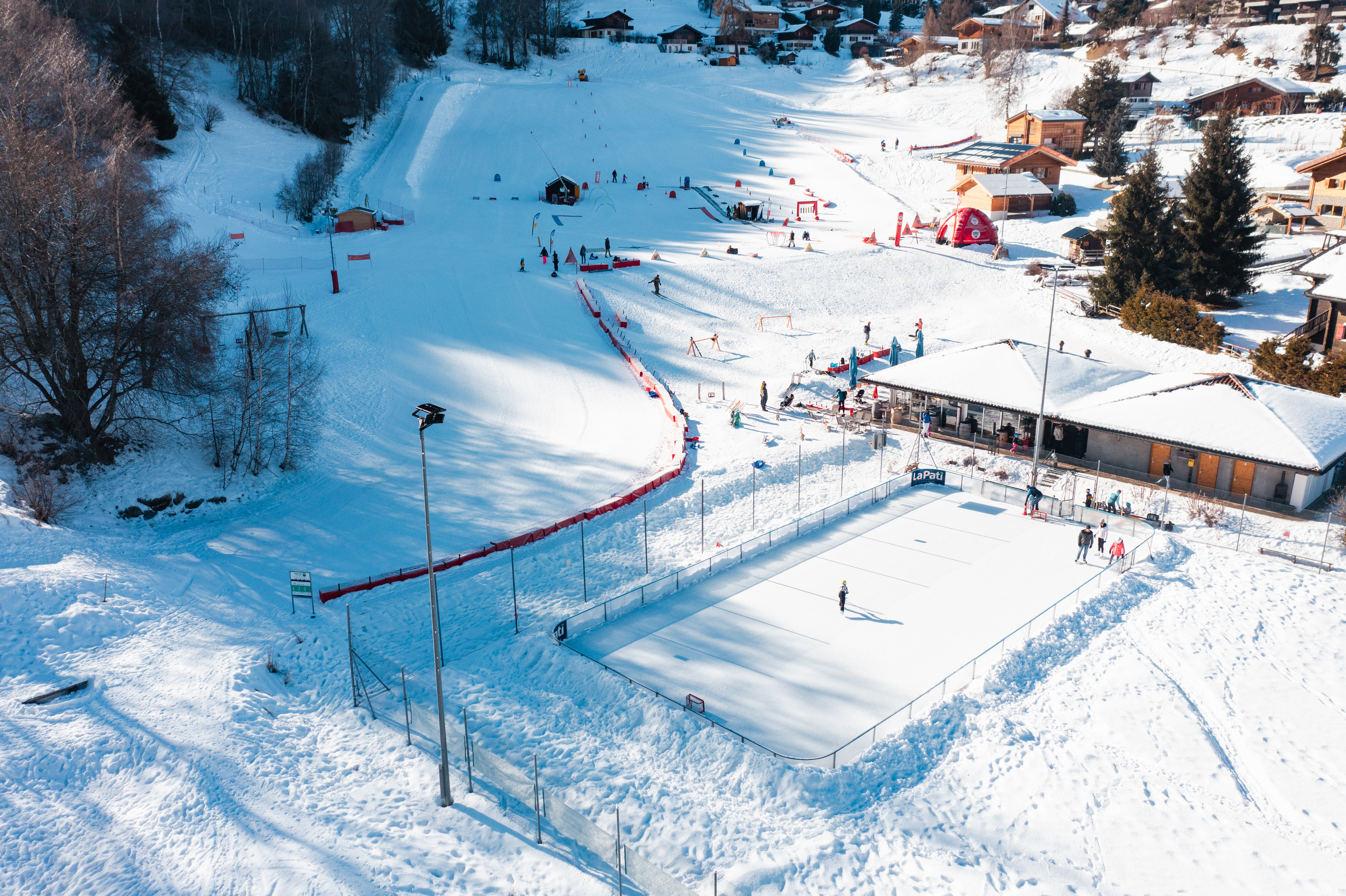 Vue aérienne de l’espace débutants Le Lavioz à Vercorin, en Valais, avec la piste de ski, le restaurant et la patinoire dans un cadre hivernal.
