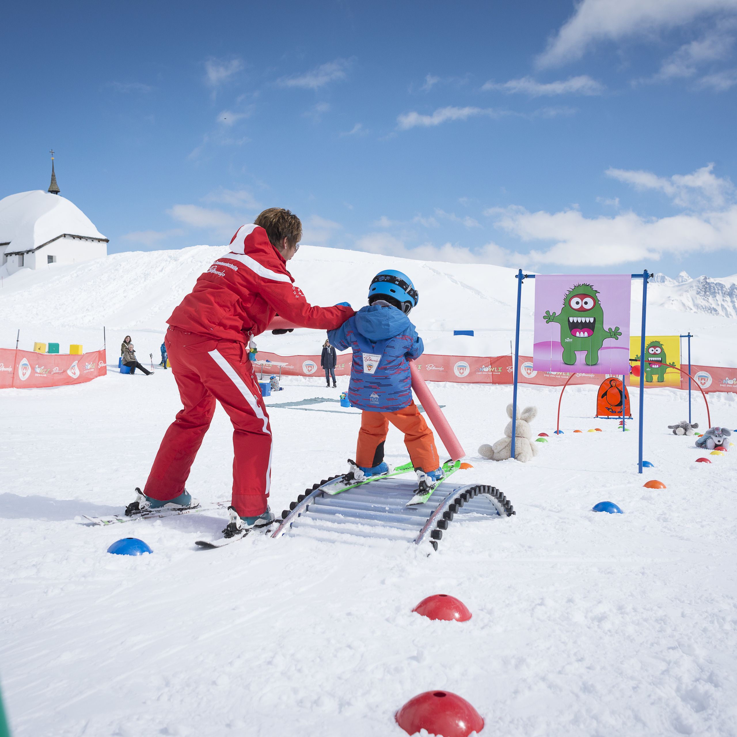 A small child learns to ski in Bettmeralp's Children's snow playground with the help of his instructor