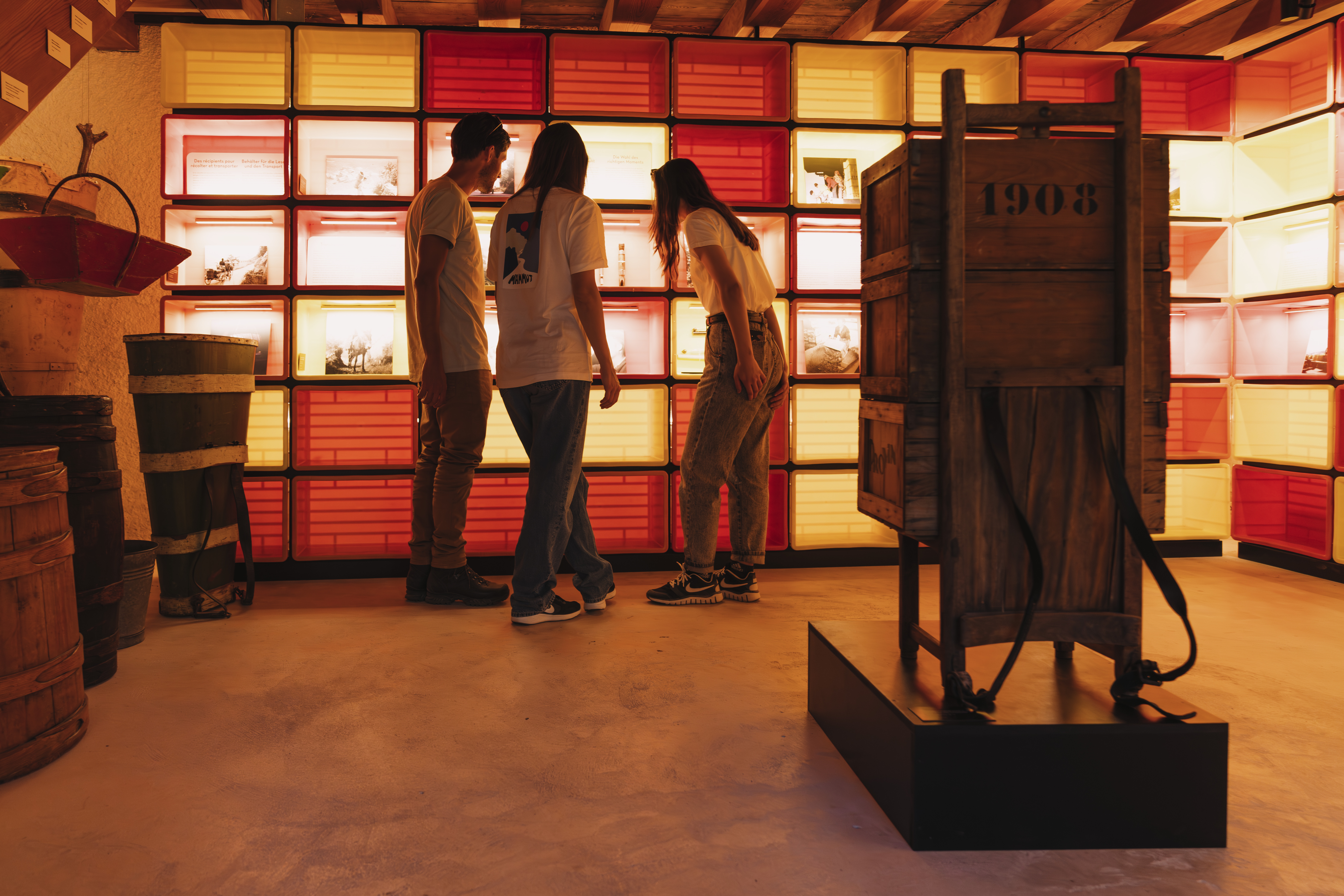 Trois personnes découvrant une exposition avec du matériel ancien et des vitrines éclairées au Musée du Vin à Salquenen, Valais, Suisse