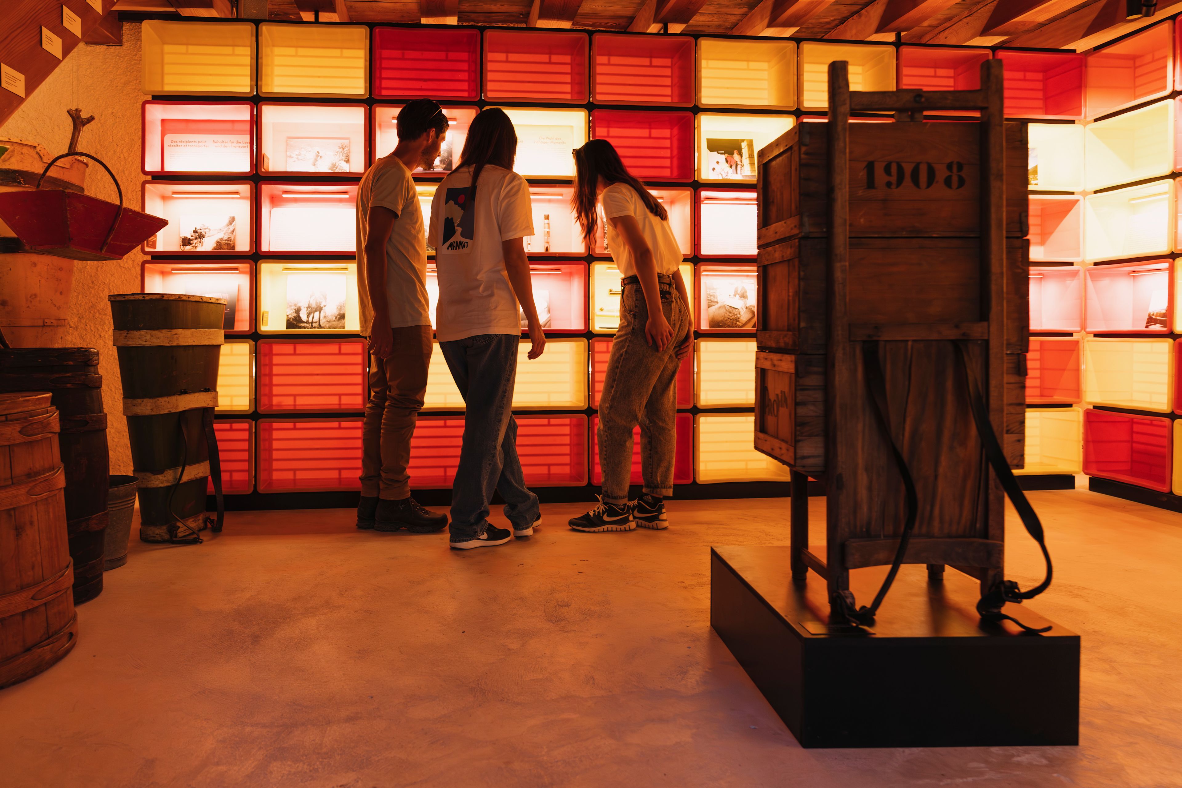 Trois personnes découvrant une exposition avec du matériel ancien et des vitrines éclairées au Musée du Vin à Salquenen, Valais, Suisse