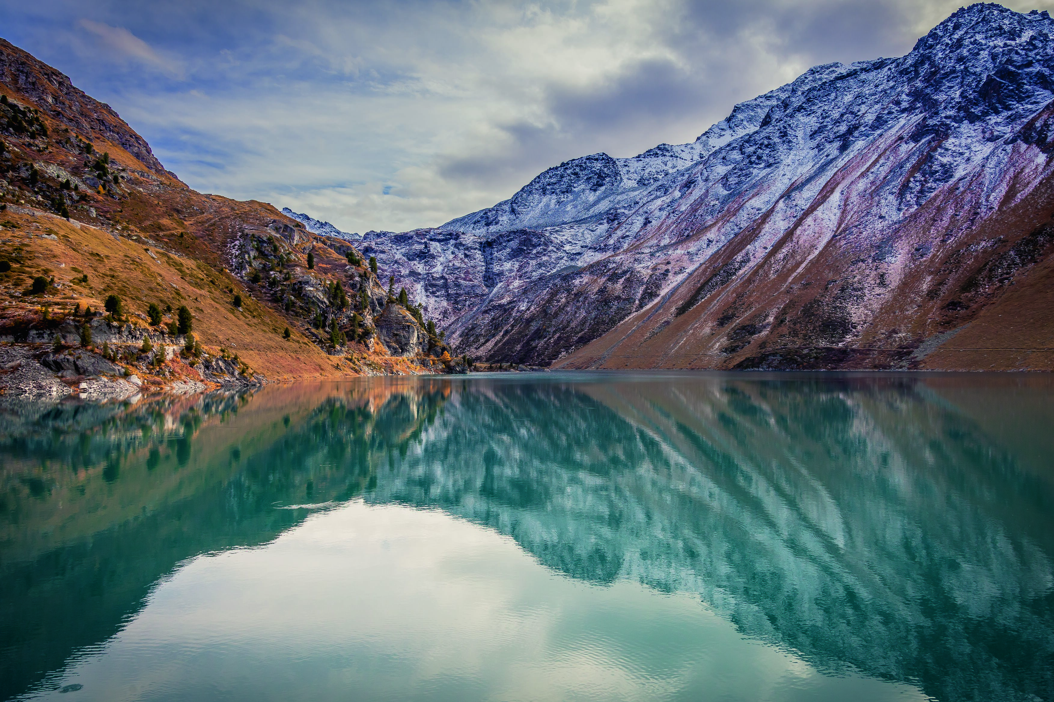 Reflection of snow-dusted mountain slopes in a clear alpine lake near Nendaz in autumn, Valais, Switzerland