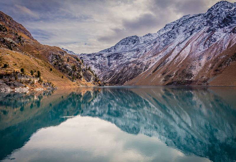 Reflection of snow-dusted mountain slopes in a clear alpine lake near Nendaz in autumn, Valais, Switzerland