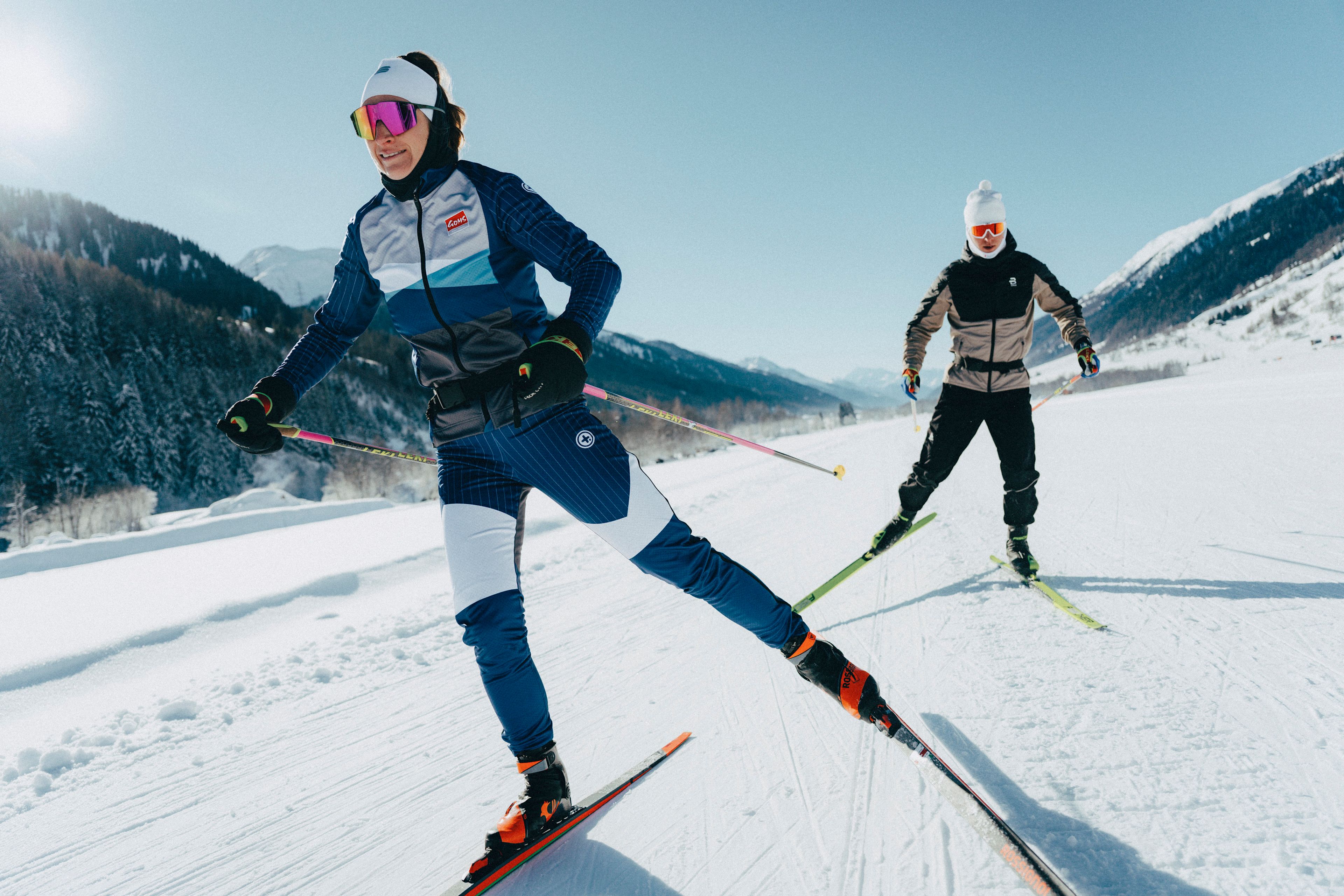 Two cross-country skiers training on the trail in the snowy landscape of Goms