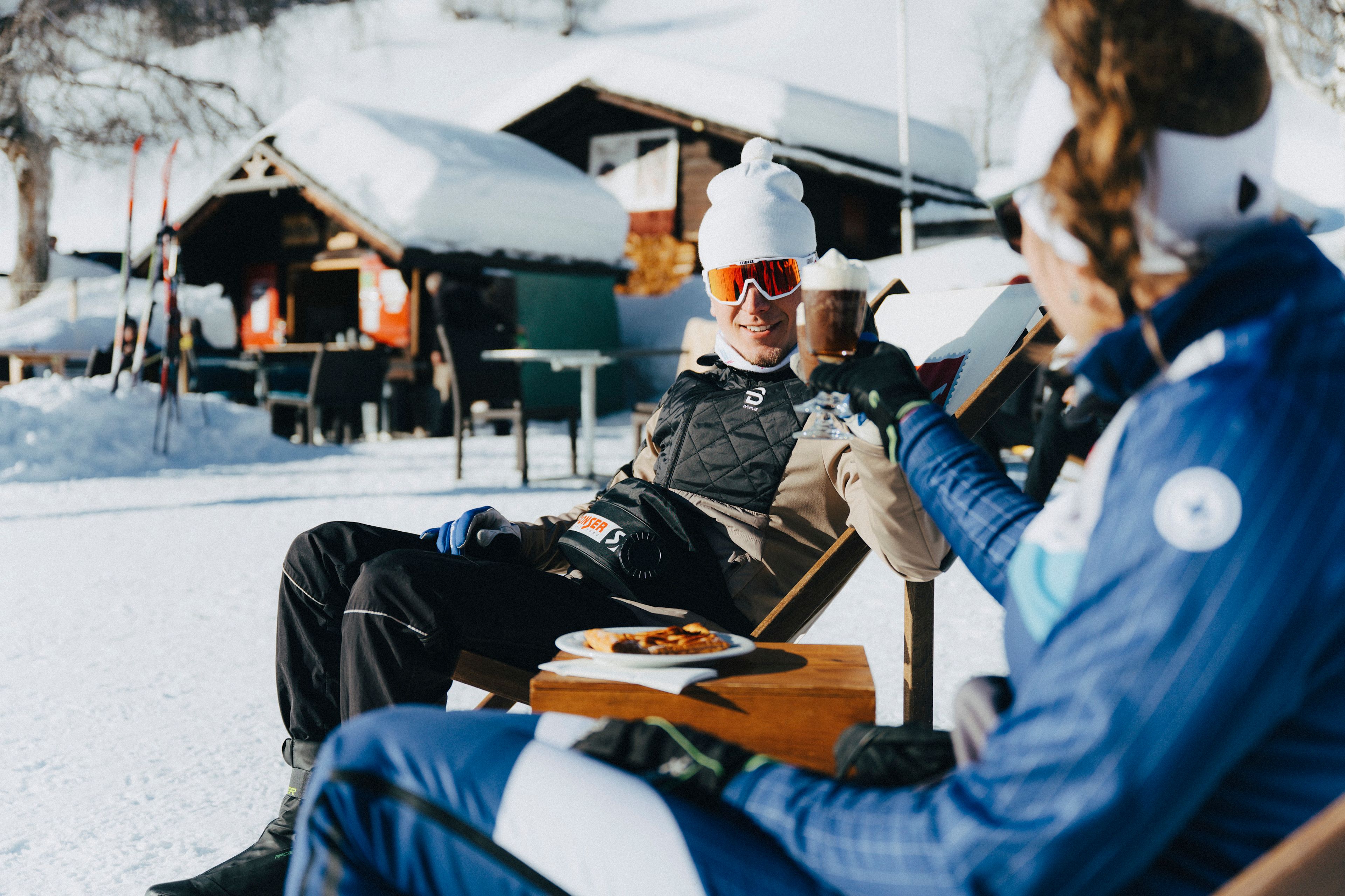 Two cross-country skiers enjoying a drink break in the sun on the Goms trail