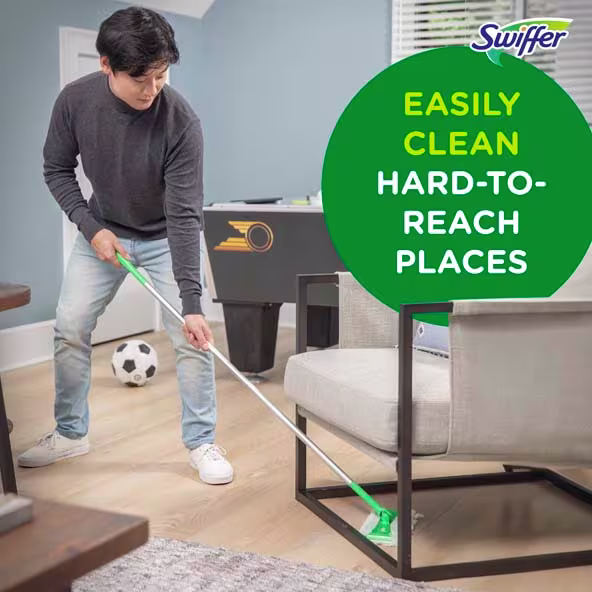 A person using a Swiffer to clean under furniture in a living room, demonstrating effective cleaning techniques