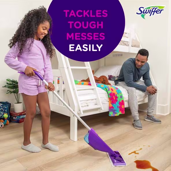 A child using a Swiffer mop to clean up a spill on the floor while an adult watches nearby
