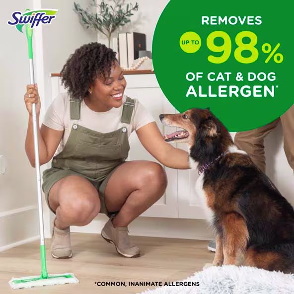 A woman smiles while using a Swiffer Sweeper near a dog, highlighting allergen and dirt removal benefits