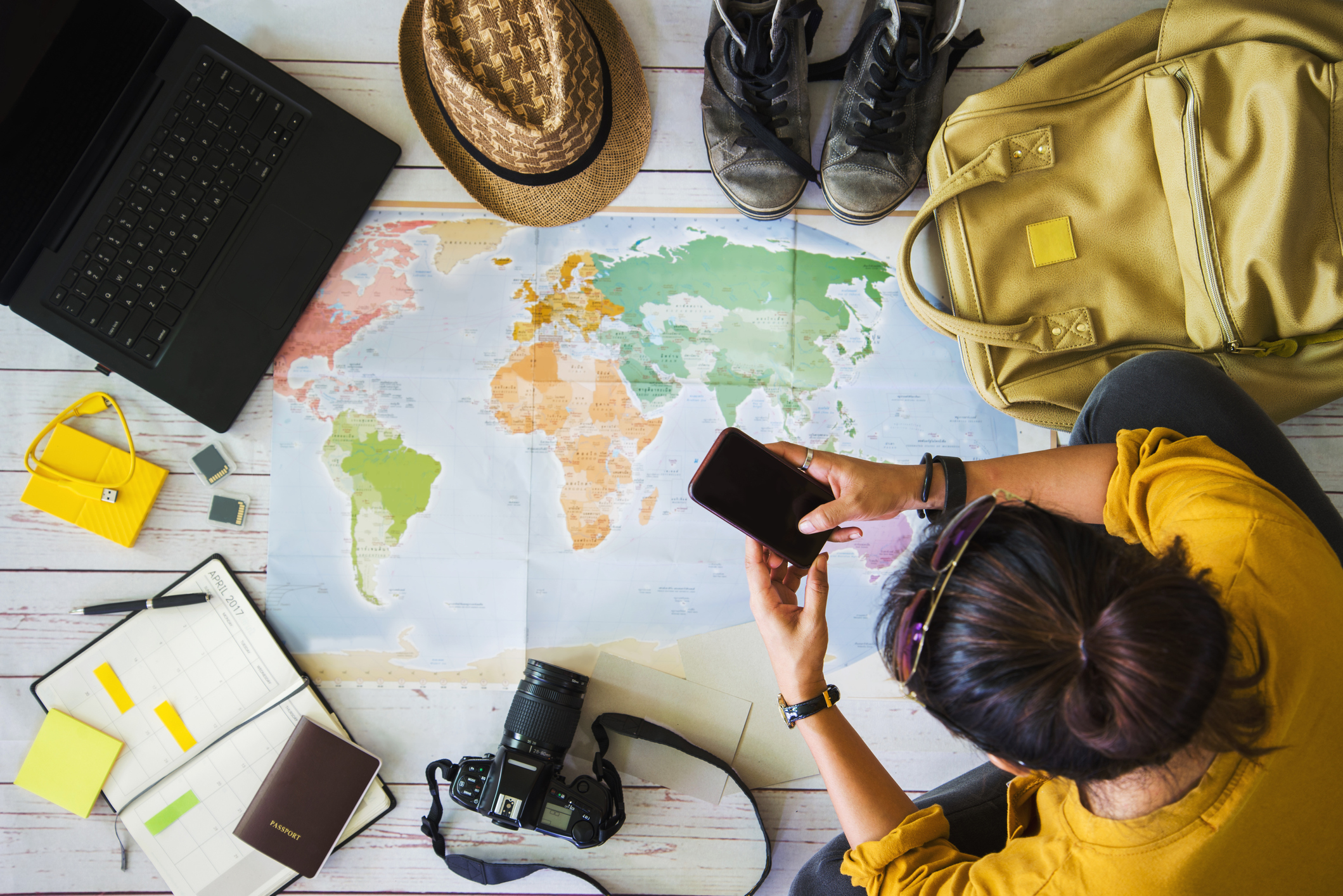 Girl planning her travels with a world map and packing essentials like notebook, camera, walking boots and backpack