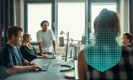 People working at a table, on laptops, with shield shape overlay
