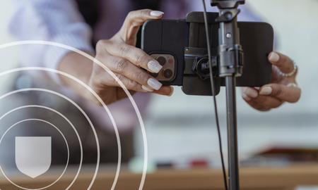 Person setting up a smartphone on a tripod, focusing on security with a shield icon overlay.