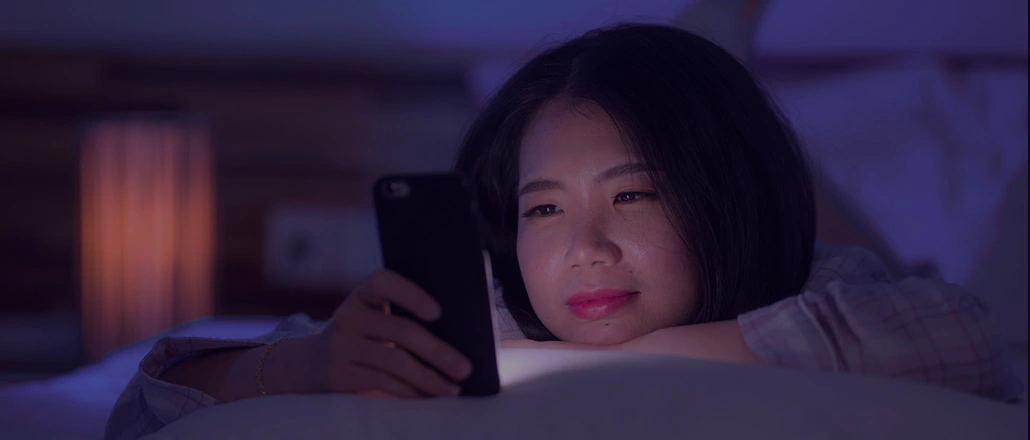 Young woman in bed on her phone at night.
