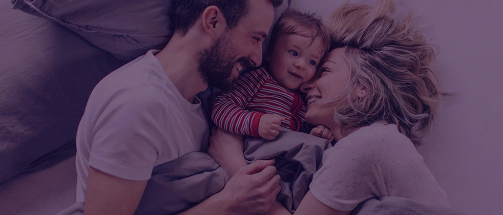 Happy couple playing with their son in bed.