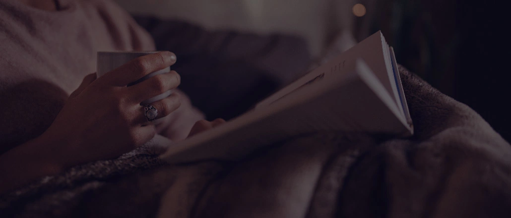 Woman reading a book in bed while drinking tea