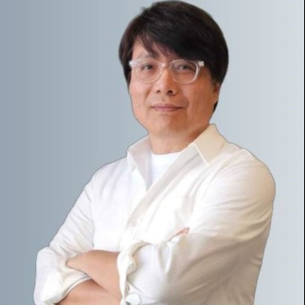 A person with dark hair and glasses is wearing a white shirt and has their arms crossed. The background is a light gray gradient.