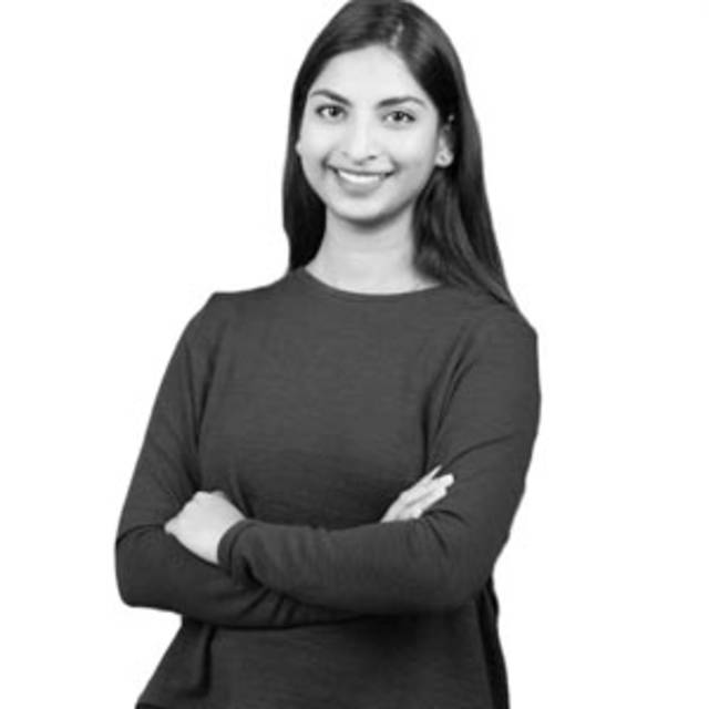 A black and white photo of a person with long hair, wearing a long-sleeve shirt, smiling with arms crossed. The background is plain white.