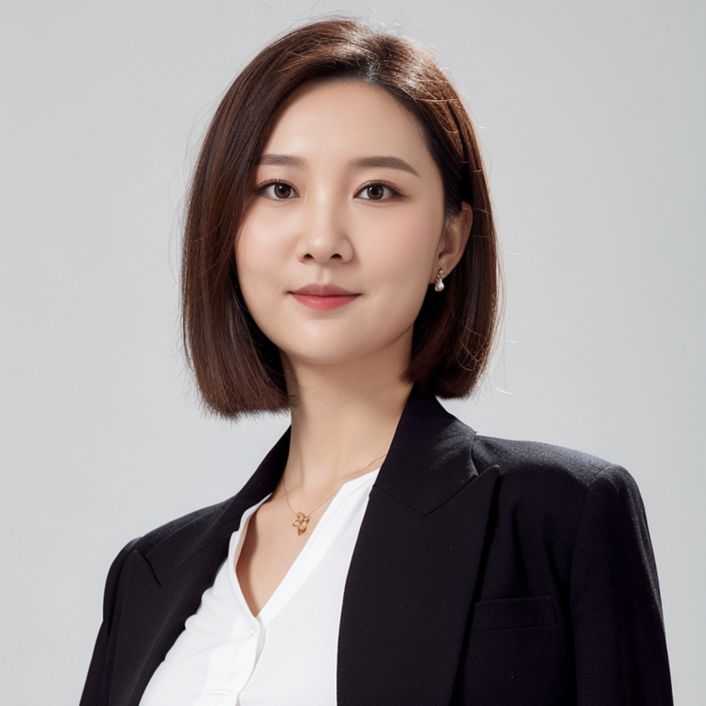 A person with short brown hair wearing a black blazer and white shirt smiles confidently against a gray background.