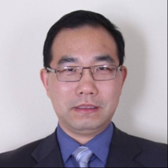 Man in a suit and tie with glasses, standing against a plain background.