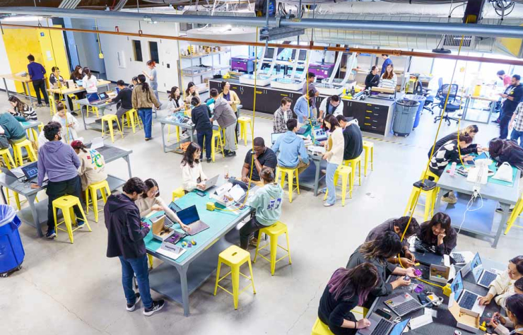 Many people working at tables on technical projects in the GIX Prototyping Labs