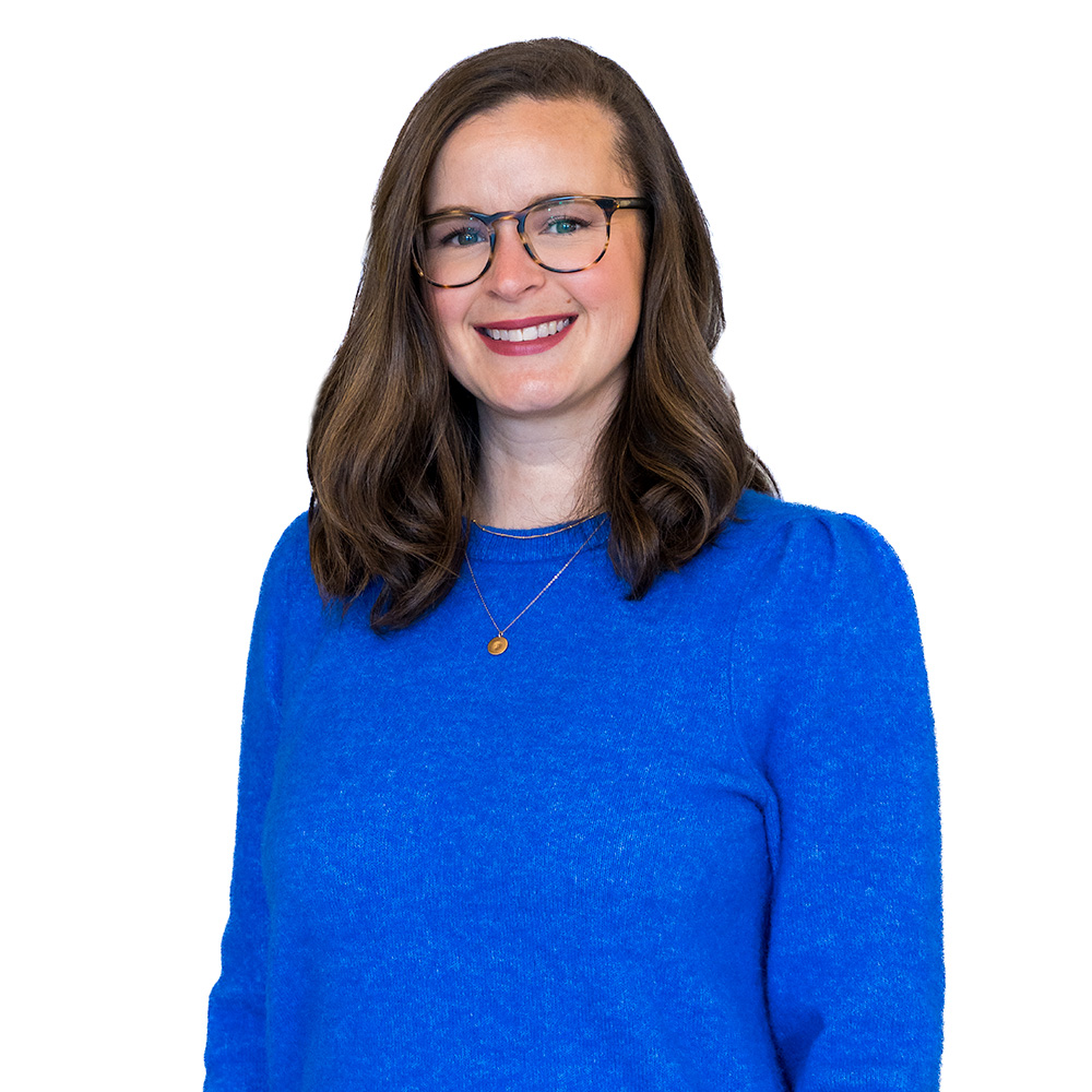 A person with long brown hair and glasses is smiling and wearing a blue sweater. The background features a pattern of repeating rectangular shapes.