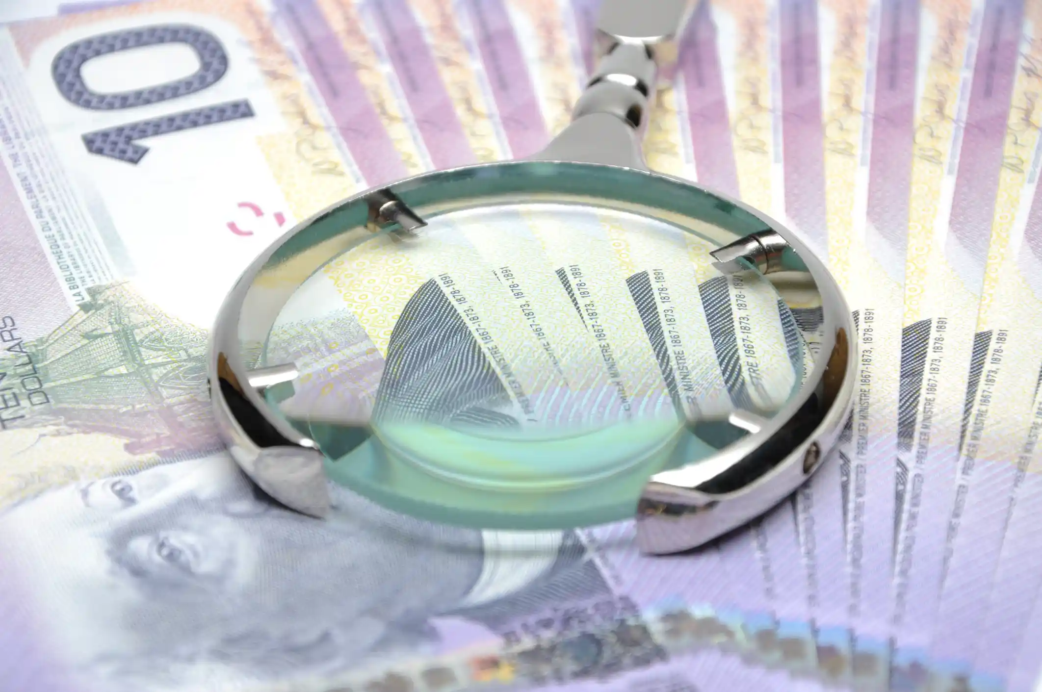Close-up of a magnifying glass placed on top of Canadian ten-dollar bills, highlighting security features and fine print on the banknotes.