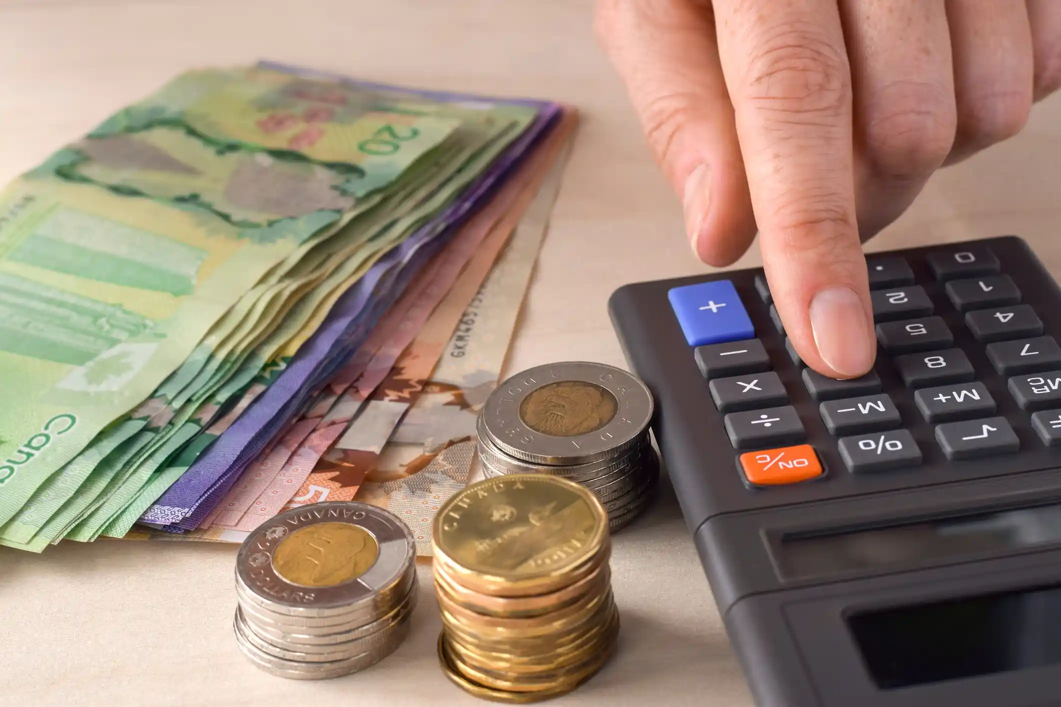 Canadian coins and banknotes beside a calculator with a person pressing a button.