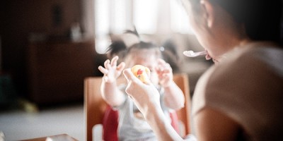 A woman feeding a child while using a toy