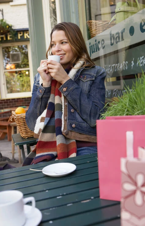 Young woman sitting outside cafe drinking coffee