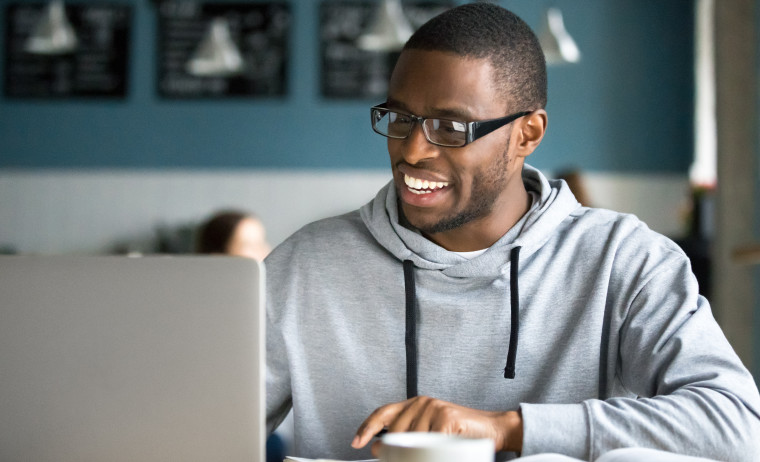 A male IELTS test taker wearing a grey hoodie and glasses prepares for IELTS on his computer