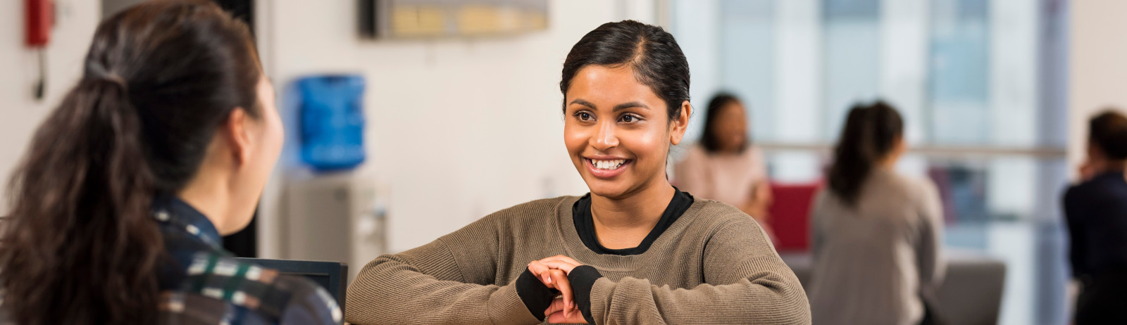 Female test taker wearing a green sweatshirt talks to an IELTS test centre staff