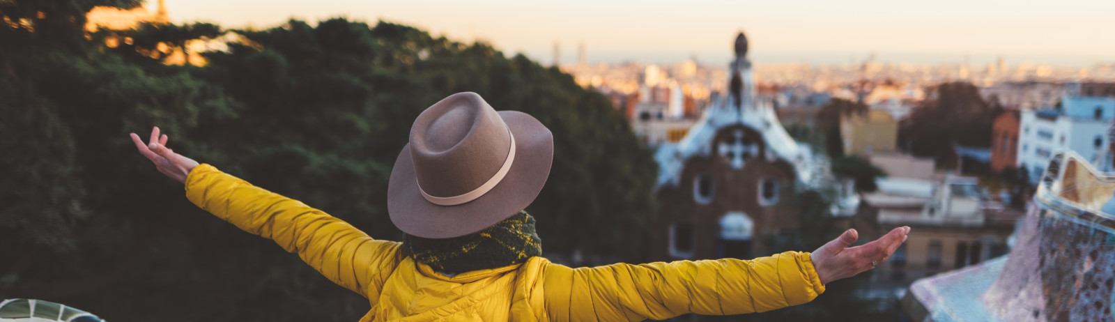A female IELTS test taker wearing yellow hoddie with hat stands at the top of a tower and enjoying the city view.