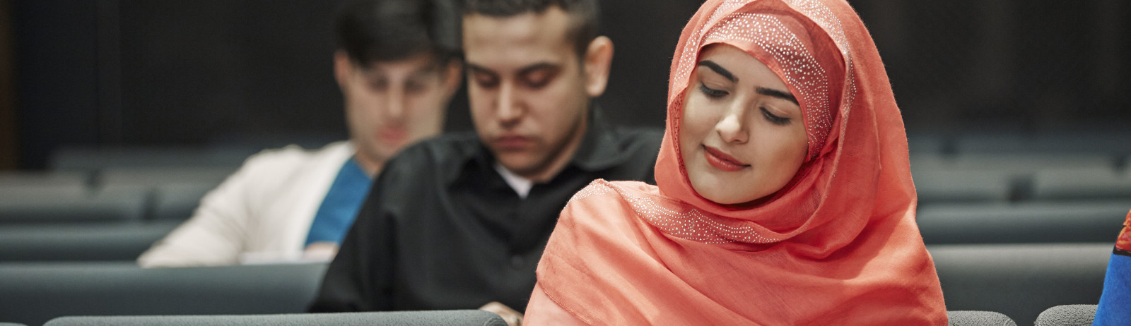A female test taker wearing a peach hijab preparing for the IELTS test along with other test takers.