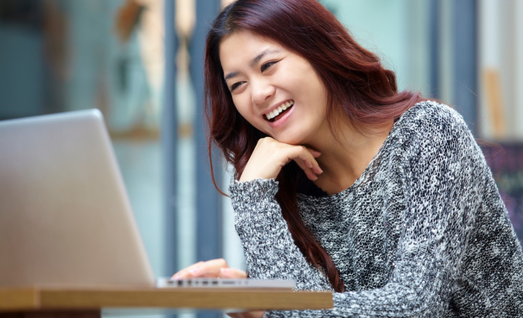 A female test taker wearing a grey top looks at her laptop and prepares for IELTS.