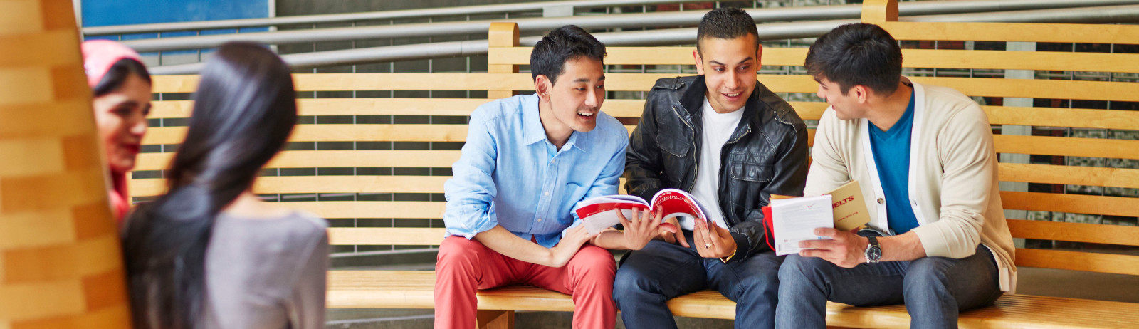 Three male IELTS test takers sitting on a bench prepare for IELTS test with the official preparation materials.