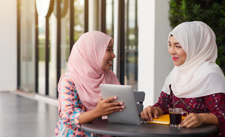 Two female IELTS test takers wearing hijabs chatting happily
