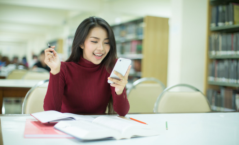 A female test taker wearing a red turtle-neck t-shirt looks at her IELTS result on her cellphone