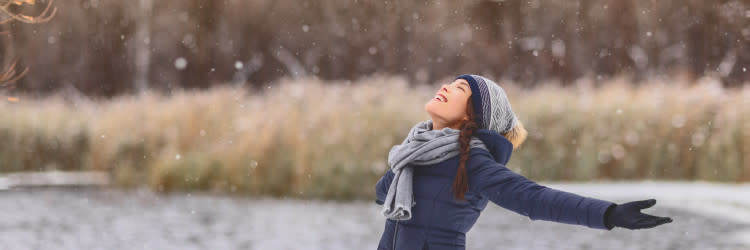 Woman in winter clothing looking up as snow falls - CANADA